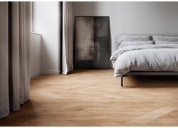 Helles Schlafzimmer mit Fischgrätparkett und grauem Bett.