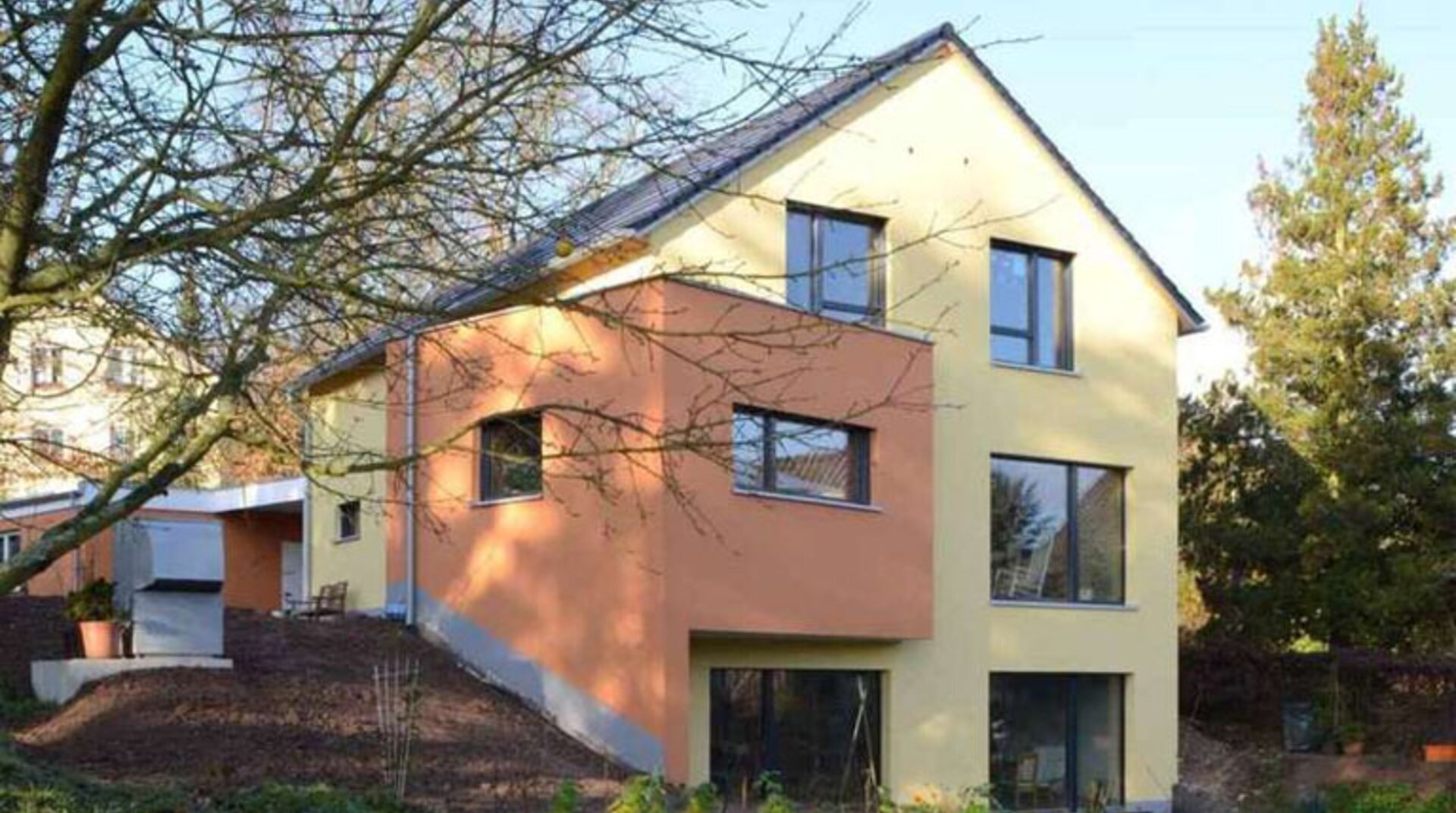 Müllers Bau Einfamilienhaus Konz Könen, Sicht auf Außenfassade, gelbes orange farbenes Haus, Blick durch blätterlose Bäume